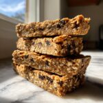 A stack of four homemade chocolate chip protein bars made with oats, sitting on a marble surface.