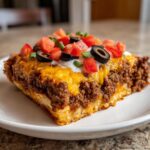 A thick slice of mexican pizza featuring seasoned ground beef, melted cheese, sour cream, diced tomatoes, and black olives.