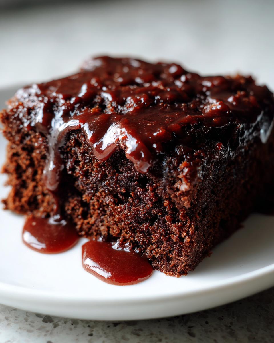 Close-up of a moist slice of dark chocolate Dr Pepper cake topped with a rich, dark glaze dripping onto a white plate.