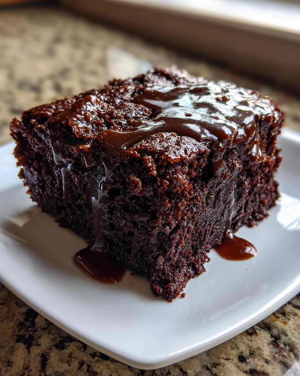 A close-up of a rich, dark slice of Dr Pepper cake topped with a glossy, dripping chocolate glaze.