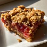 A close-up of a square slice of Old-Fashioned Rhubarb Crunch showing the bright red filling and crumbly oat topping.