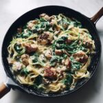 Overhead view of creamy chicken spinach pasta with seared chicken pieces in a black skillet.