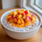 A white bowl filled with creamy peach chia pudding, topped with diced peaches and a sprinkle of cinnamon.