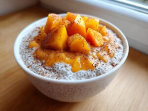 A white bowl filled with creamy peach chia pudding, topped with diced fresh peaches and a sprinkle of cinnamon.