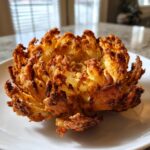 A perfectly cooked, golden-brown blooming onions appetizer served on a white plate.