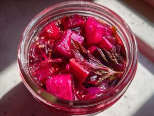 Overhead view of a glass jar filled with vibrant magenta Pickled Rhubarb with Red Shiso pieces and brine.