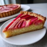 Close-up of a slice of Rhubarb and Almond Chevron Tart showing bright pink rhubarb arranged over a golden almond frangipane base.