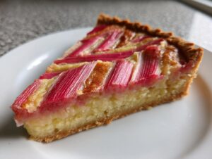 A close-up slice of Rhubarb and Almond Chevron Tart showing bright pink rhubarb stalks arranged decoratively over a golden almond frangipane filling.