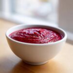 Close-up of vibrant, deep red Rhubarb and Beetroot Ketchup served in a small white bowl.