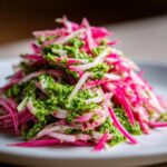 Close-up of vibrant Rhubarb and Fennel Slaw tossed generously with bright green Chimichurri sauce on a white plate.