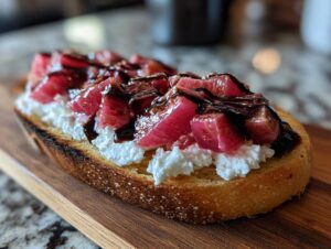 A single piece of Rhubarb and Goat Cheese Bruschetta featuring toasted bread, creamy goat cheese, pink rhubarb pieces, and a balsamic glaze drizzle.