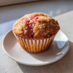 A single, freshly baked Rhubarb and Pecan Muffin topped with coarse sugar, sitting on a small white plate.