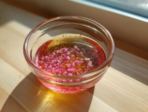 A small glass bowl containing the pink and golden Rhubarb and Shallot Vinaigrette with finely diced pink ingredients floating on top.