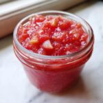 Close-up of chunky, bright red rhubarb cinnamon jam filling a small glass jar.