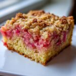 Close-up of a square slice of Rhubarb Sour Cream Cake with Nutmeg, showing pink rhubarb filling and a golden crumb topping.