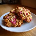 Three freshly baked Rhubarb White Chocolate Oatmeal Cookies stacked slightly on a small white plate.