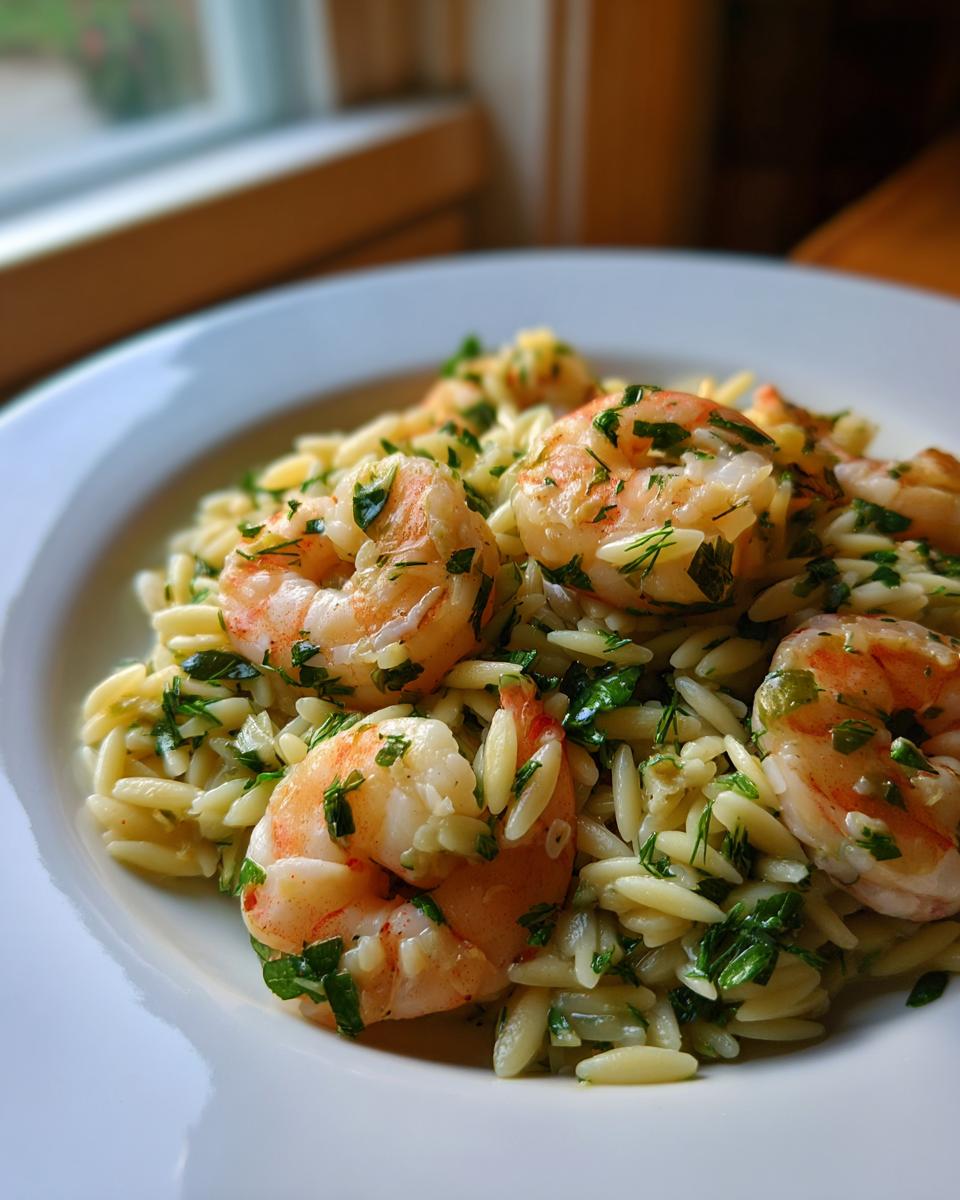Close-up of a white bowl filled with bright shrimp orzo salad, topped with fresh herbs.