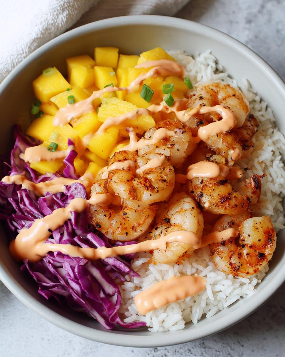 Close-up of perfectly seasoned shrimp rice bowls featuring white rice, grilled shrimp, diced mango, and purple cabbage.