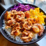 Close-up of flavorful shrimp rice bowls topped with seasoned shrimp, mango chunks, red cabbage, and spicy sauce.