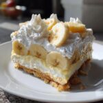 A delicious slice of banana pudding featuring layers of crust, custard, fresh banana slices, and topped with whipped cream.