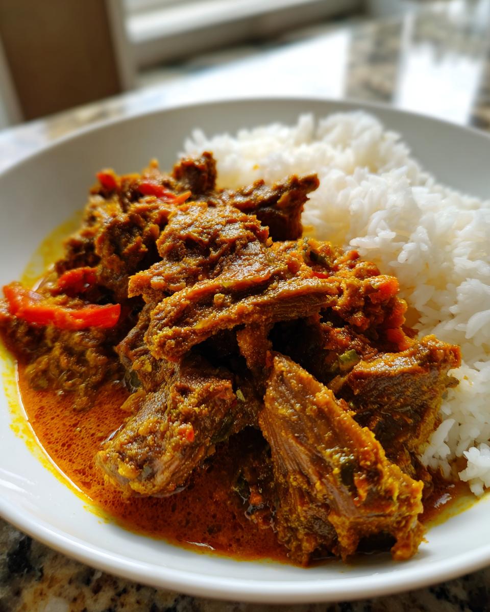 Close-up of tender pieces of slow cooker lamb curry coated in rich, orange sauce served next to a mound of fluffy white rice.
