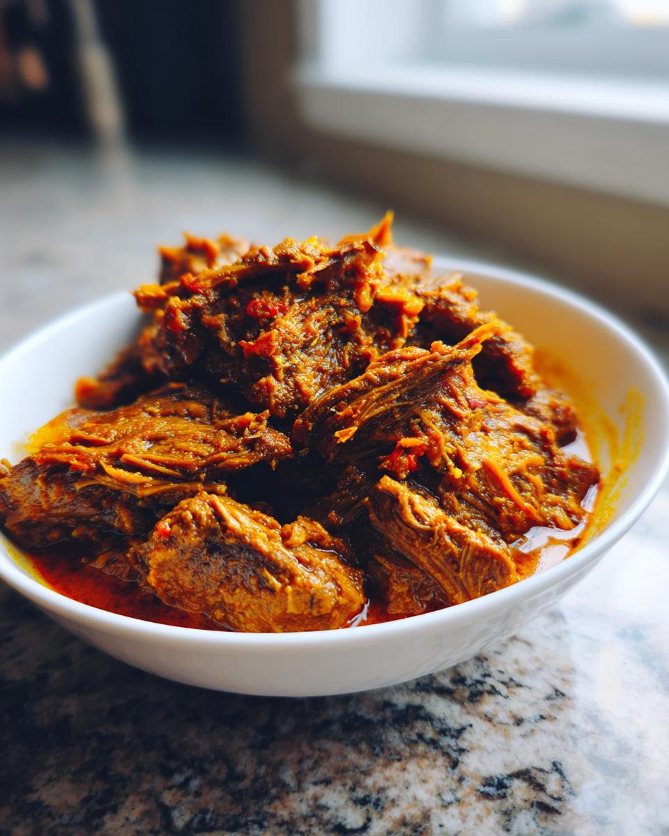 Close-up of tender, shredded meat in a rich, orange-red sauce, representing slow cooker lamb curry.