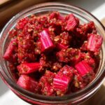Close-up of bright pink rhubarb pieces coated in red chili paste for Small-Batch Rhubarb Kimchi in a glass jar.