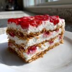 A layered slice of strawberry dream dessert with graham cracker crust, cream filling, and strawberry topping.