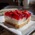 A close-up of a perfectly layered slice of strawberry pretzel salad showing the crust, cream cheese layer, and strawberry topping.