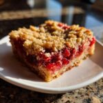 Close-up of a square slice of Strawberry Rhubarb Buckle with Ginger Crumb topping on a white plate.