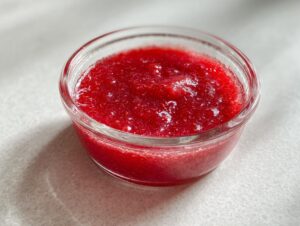 Close-up of vibrant red Strawberry Rhubarb Pineapple Jam served in a small, clear glass bowl.