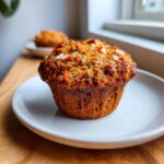 A close-up of a freshly baked morning glory muffin topped with nuts and visible shredded carrots.