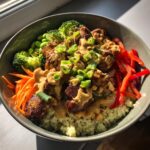 A vibrant thai peanut chicken buddha bowl featuring crispy chicken, quinoa, broccoli, carrots, peppers, and peanut sauce.