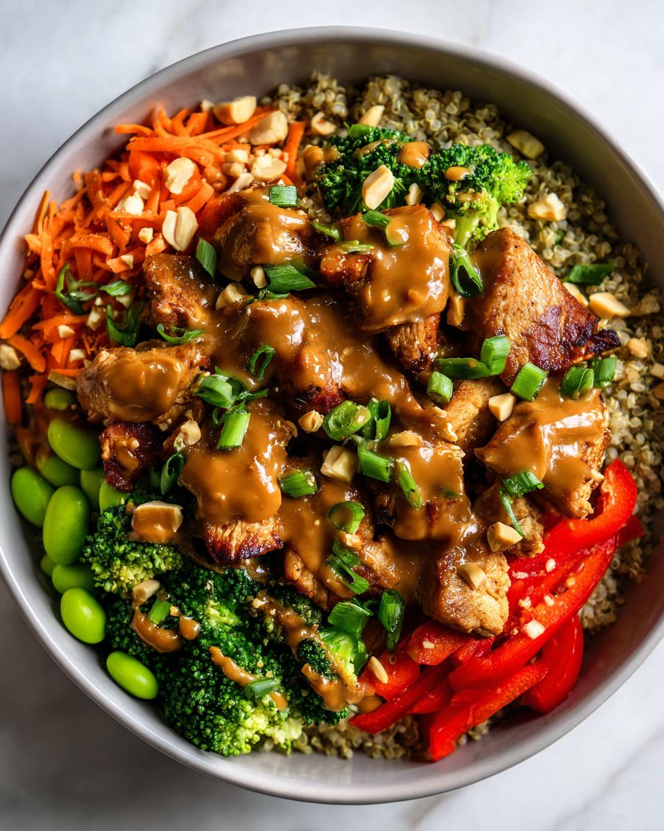 Overhead view of a vibrant thai peanut chicken buddha bowl featuring chicken, quinoa, broccoli, carrots, and peanut sauce.