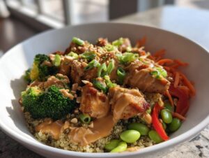 Close-up of a vibrant thai peanut chicken buddha bowl featuring quinoa, chicken, broccoli, edamame, and peanut sauce.