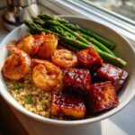 A close-up of a healthy tofu and shrimp protein bowl served over quinoa with roasted asparagus.