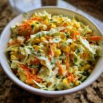 A close-up view of creamy zesty corn coleslaw featuring shredded cabbage, bright yellow corn kernels, and shredded carrots.