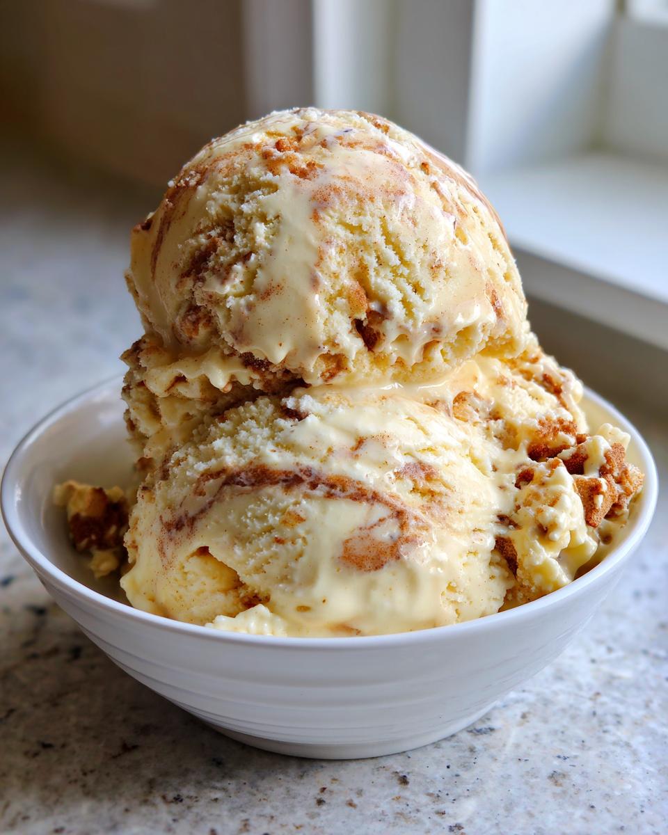 Two scoops of creamy apple pie ice cream swirled with cinnamon and pie crust pieces in a white bowl.