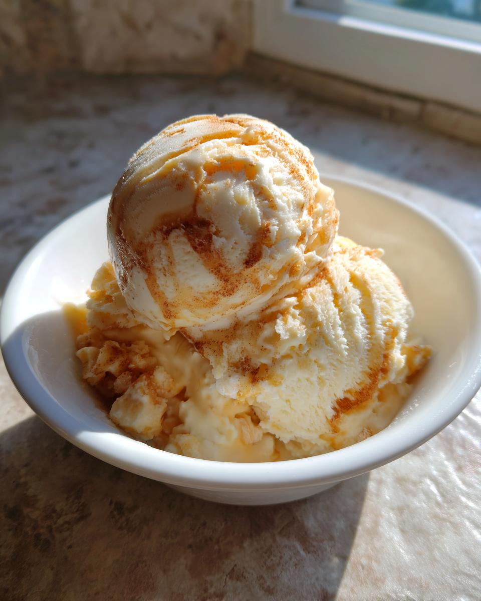 Two scoops of creamy apple pie ice cream topped with a cinnamon swirl served in a white bowl.