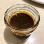 Close-up overhead shot of rich, dark balsamic vinaigrette dressing in a small glass jar.