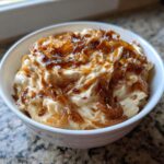 Close-up of creamy, rich caramelized french onion dip topped with glossy, dark caramelized onions in a white bowl.