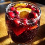 Close-up of a glass filled with bubbling cranberry sangria, garnished with fresh cranberries and orange slices.