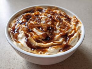 A close-up of creamy caramelized french onion dip swirled with rich, dark caramelized onions in a white serving bowl.