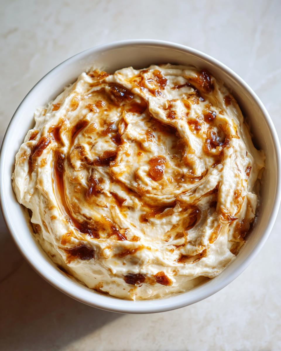 Overhead view of creamy caramelized french onion dip swirled with rich, dark caramelized onions in a white serving bowl.