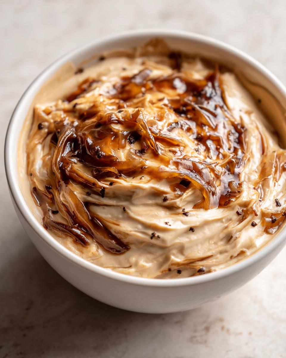 Close-up of creamy caramelized french onion dip topped with glossy, dark caramelized onions in a white bowl.