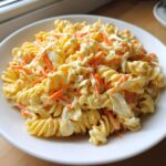Close-up of creamy coleslaw pasta salad featuring fusilli pasta, shredded carrots, and cabbage in a rich dressing.