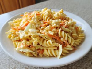 A close-up of creamy coleslaw pasta salad featuring rotini pasta, shredded carrots, and cabbage in a rich dressing.