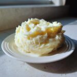 A mound of fluffy, creamy low calorie mashed potatoes served on a small white ridged plate, highlighted by natural light.