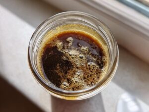 Overhead view of freshly mixed balsamic vinaigrette dressing with small bubbles in a clear glass jar.