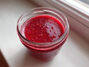 Overhead view of bright red, slightly textured raspberry vinaigrette stored in a small glass jar.